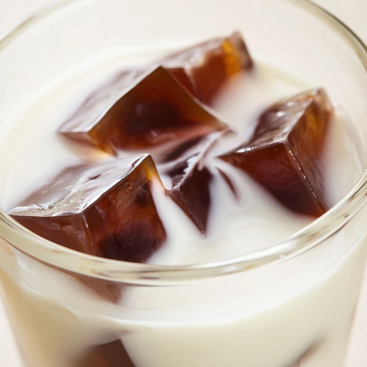 This photo shows a glass of refreshing Coffee Jelly Drink filled with glistening, bouncy coffee jelly cubes, all suspended in a creamy, light-colored milk mixture.  