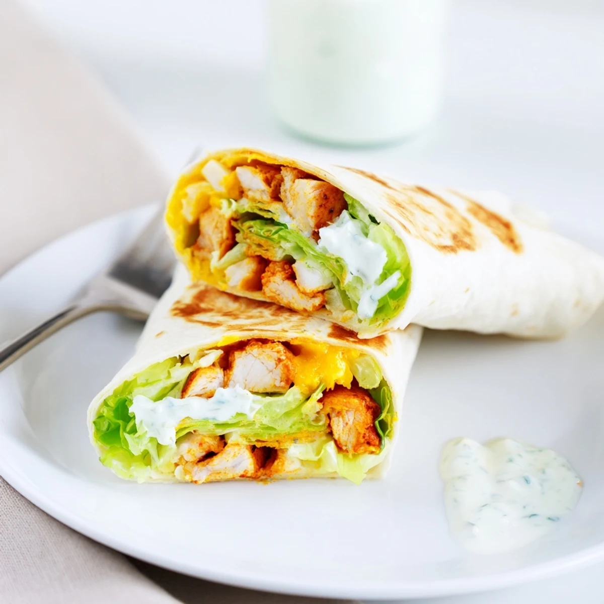 A close-up of a Buffalo Ranch Chicken Wrap, sliced in half to reveal juicy buffalo chicken, melted cheddar, and crisp romaine lettuce inside a golden tortilla.