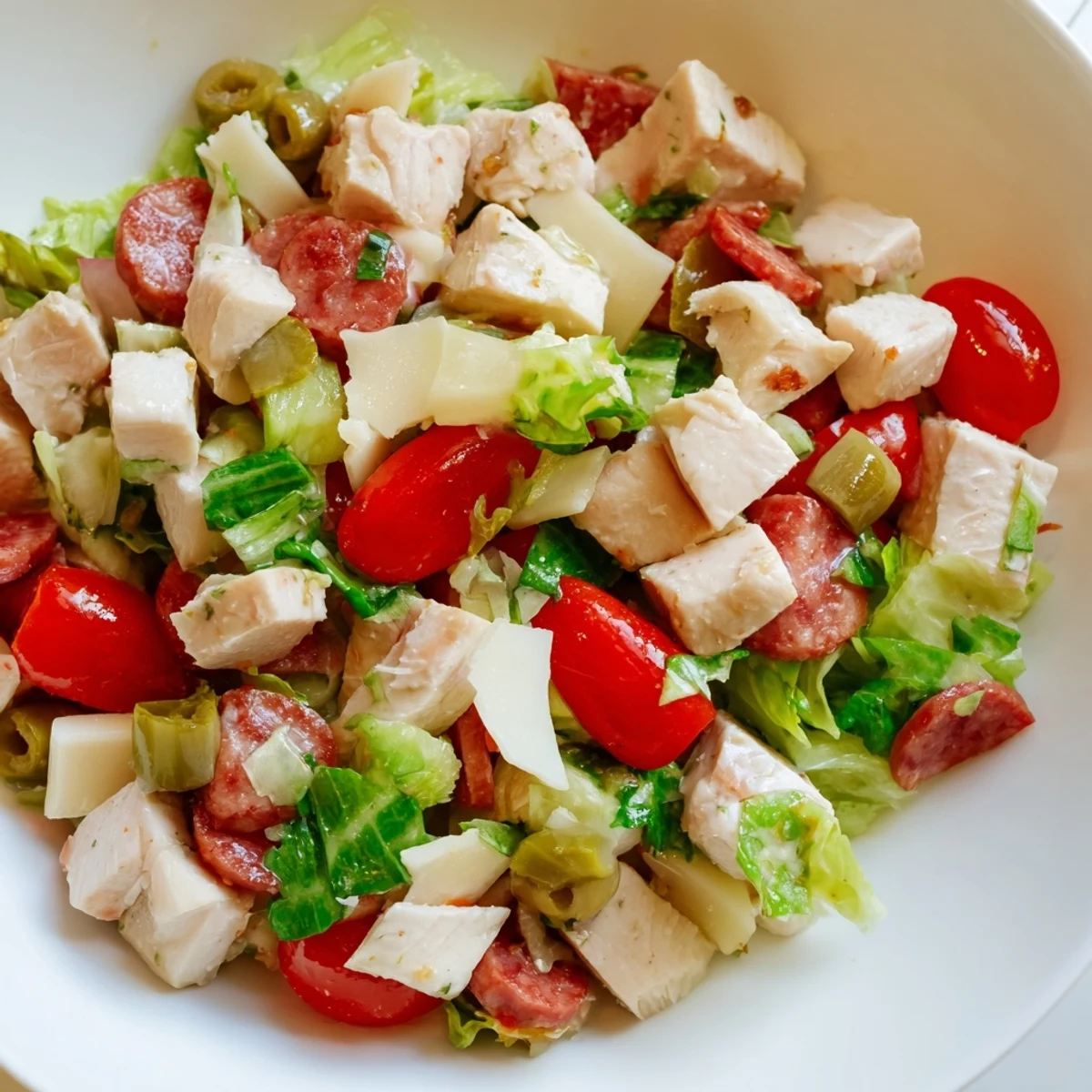 A close-up of Italian Deli Chopped Chicken Salad features chopped chicken, salami, and provolone on crisp romaine lettuce with tomatoes and red onion.