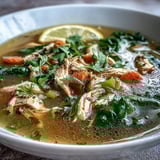 Golden High Protein Lemon and Turmeric Chicken Soup steaming in a white bowl with fresh parsley and lemon wedges.