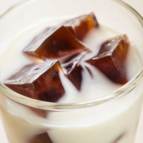 This photo shows a glass of refreshing Coffee Jelly Drink filled with glistening, bouncy coffee jelly cubes, all suspended in a creamy, light-colored milk mixture.  