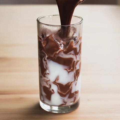 A tall glass of Milo Ice Latte Hack with ice cubes, chocolatey malt powder, and creamy milk swirling together for a refreshing summer drink.  