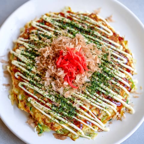 A close-up view of a delicious Okonomiyaki pancake, with visible cabbage and savory toppings ready to eat.