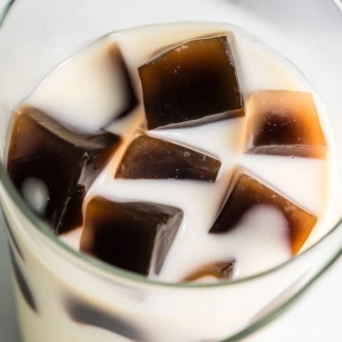 Spoonfuls of sweet Coffee Jelly Drink with translucent coffee jelly cubes rest in a creamy white milk blend, ready for a refreshing afternoon treat.  