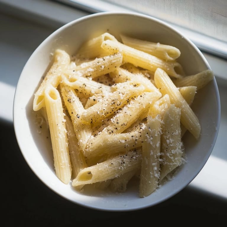 Close-up of a single-serving microwave pasta dish, showing tender spirals coated in oil and cheese, ideal for a busy solo dinner.