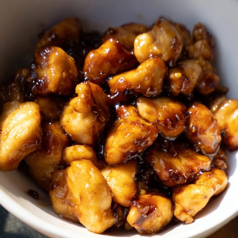 A serving of sweet chili chicken bowl features glossy, tangy sauce drizzled over vibrant vegetables and grains.